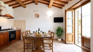 A dining area with a wooden table, chairs, a potted plant, and a TV mounted on the wall. - Apartment "Pugnano Alto - Tartufo" with Shared Pool and Wi-Fi (lisciano niccone)