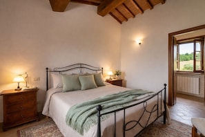 Une chambre à coucher avec un lit, des tables de chevet, une fenêtre et une vue sur la verdure.