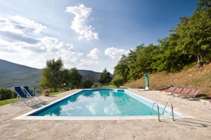 Une piscine rectangulaire à l’eau d’un bleu limpide, entourée de chaises longues et d’une terrasse en pierre.