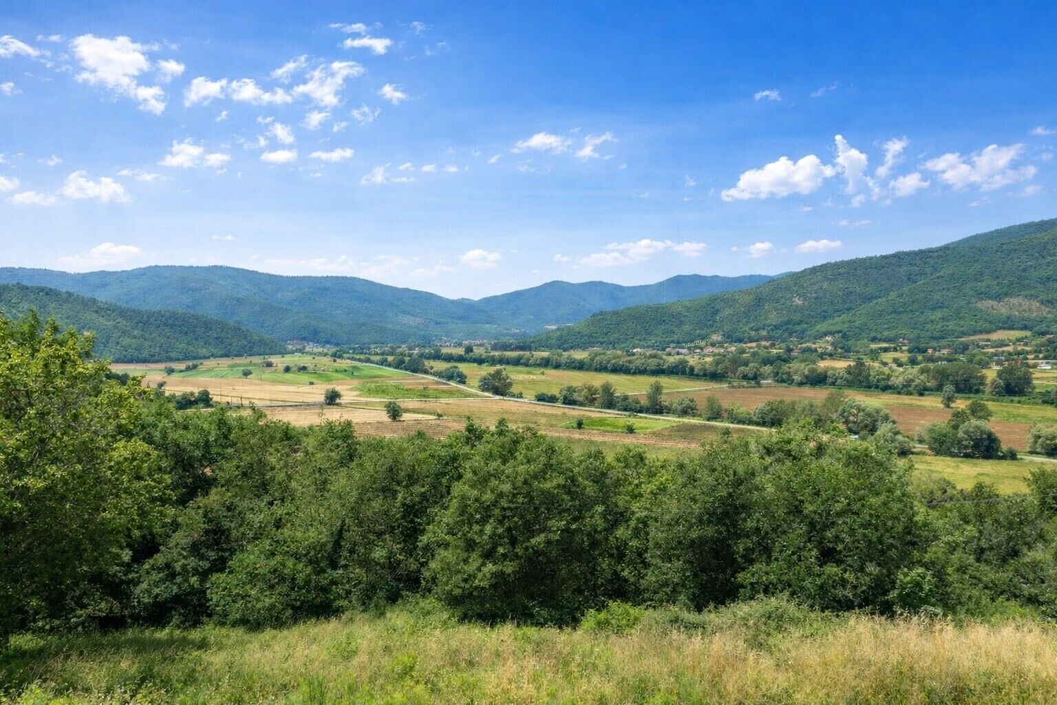 A rural landscape with rolling hills, fields, and a clear sky.
