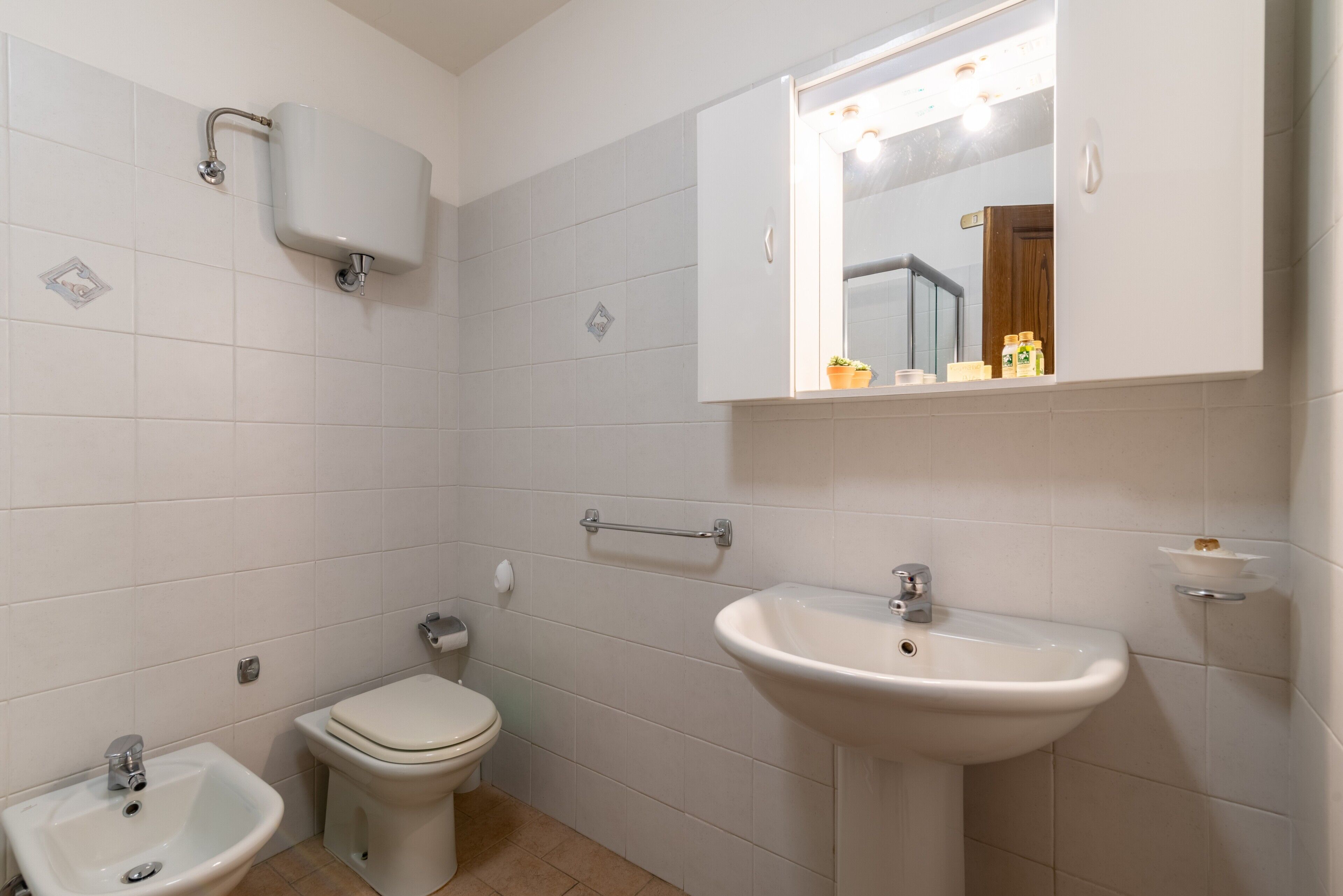 A bathroom with a toilet, bidet, sink, and a mirror above the sink.