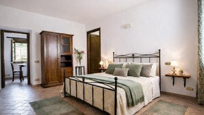 A bedroom with a bed, bedside tables, a wardrobe, and a door leading to another room. - Apartment "Pugnano Alto - Grano" with Shared Pool and Wi-Fi (Lisciano Niccone)