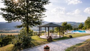 A gazebo with outdoor seating, a swimming pool, and a view of distant hills. - Apartment "Pugnano Alto - Grano" with Shared Pool and Wi-Fi (Lisciano Niccone)