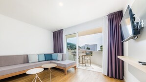 Ein modernes Wohnzimmer mit einer Couch, zwei kleinen Tischen, einem Fernseher und einem Balkon mit Vorhängen.