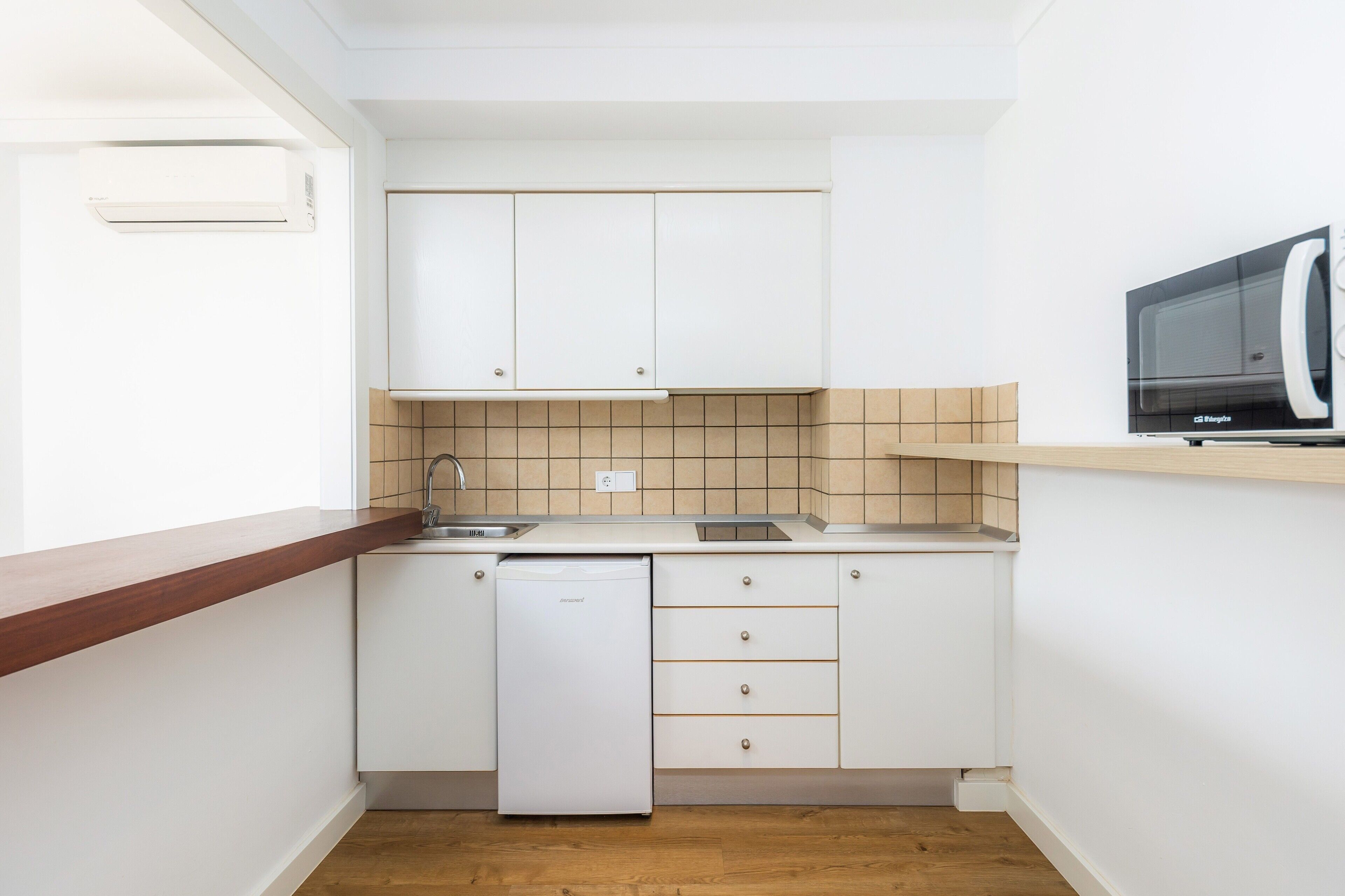Una cucina compatta con mobili bianchi, lavastoviglie, forno a microonde e piano di lavoro in legno.