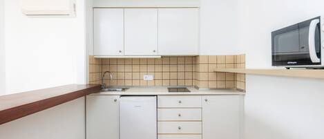 Una cucina compatta con mobili bianchi, lavastoviglie, forno a microonde e piano di lavoro in legno.