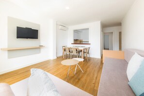 A modern living room with a flat-screen TV, a dining area with chairs and a table, and a sofa.