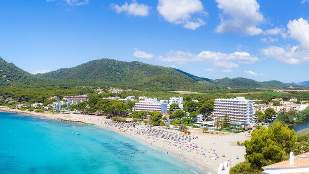 Eine Küstenstadt mit Strand, Hotelgebäuden und grünen Hügeln im Hintergrund.