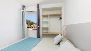 Ein Schlafzimmer mit einem Bett, einer blauen Matte, einem Kleiderschrank und Blick auf Gebäude durch eine Tür.