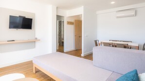 Ein modernes Wohnzimmer mit einer Couch, einem an der Wand montierten Fernseher, einem Esstisch mit Stühlen und einer Klimaanlage.
