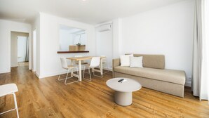 A modern living room with a wooden floor, a beige sofa, a round coffee table, and a dining area with white chairs and a wooden table. - Apartment 'Apartament Massanet 1c' with Balcony, Wi-Fi and Air Conditioning (Canyamel)