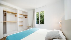 A bedroom with a bed, a window with a view of greenery, a wardrobe with hanging space, and a chair. - Apartment 'Apartament Massanet 1c' with Balcony, Wi-Fi and Air Conditioning (Canyamel)