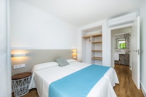 A bedroom with a bed, bedside table, wall-mounted light, and an open door leading to a bathroom.