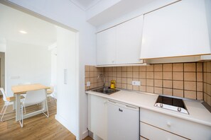 A compact kitchen with a sink, stove, and white cabinetry.