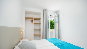 Een slaapkamer met een bed, een kledingkast, een nachtkastje en een raam met uitzicht op groen.
