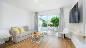 Een moderne woonkamer met een bank, een salontafel, een aan de muur bevestigde televisie en een balkon met een tafel en stoelen.