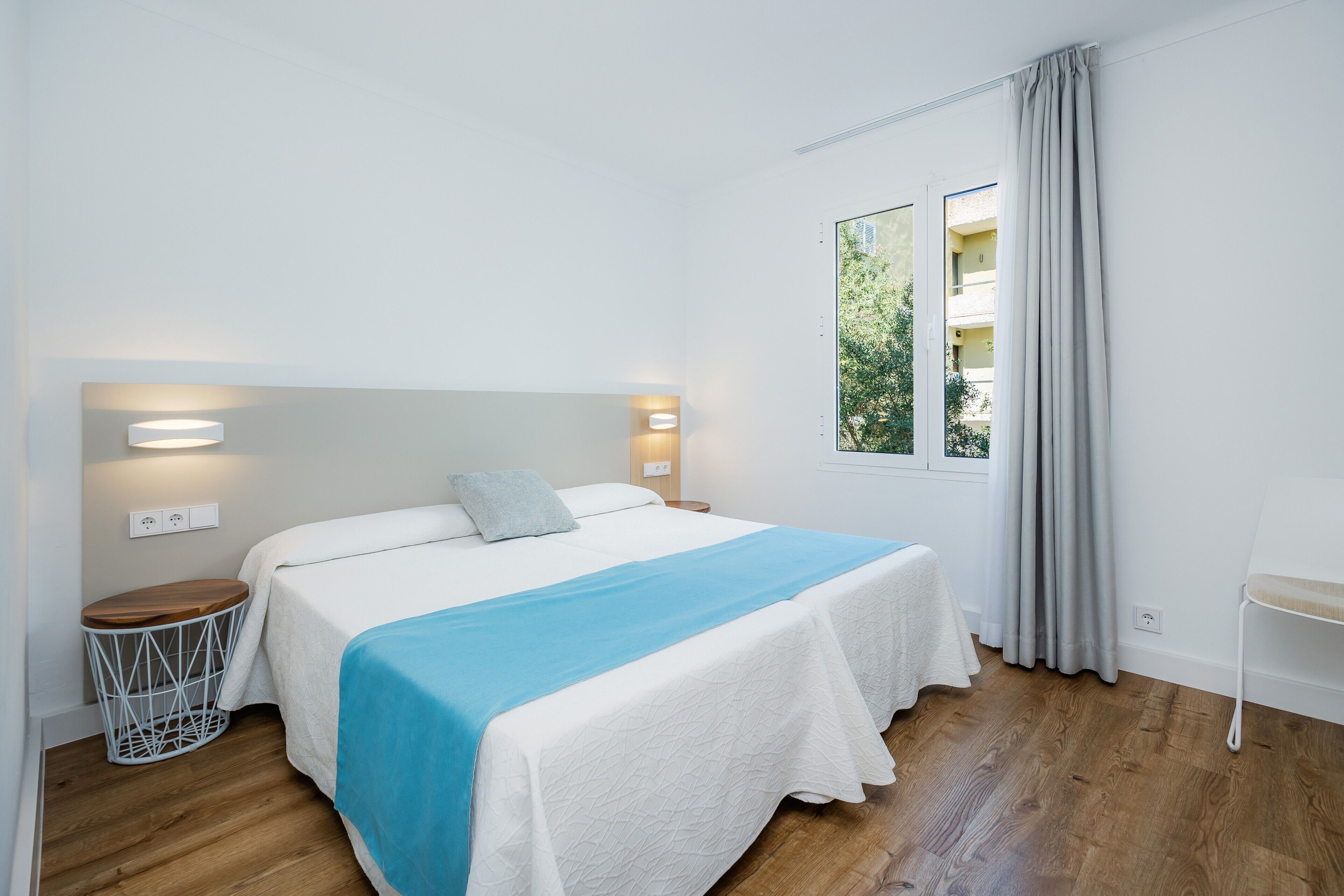 A bedroom with a bed, bedside table, lamp, and window with curtains.