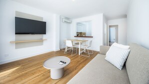 Una sala de estar moderna con un televisor de pantalla plana, una mesa redonda, un sofá y un comedor con sillas y una mesa.