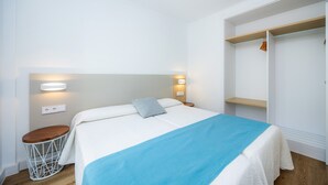Un dormitorio con cama, mesitas de noche, armario e iluminación en la pared.