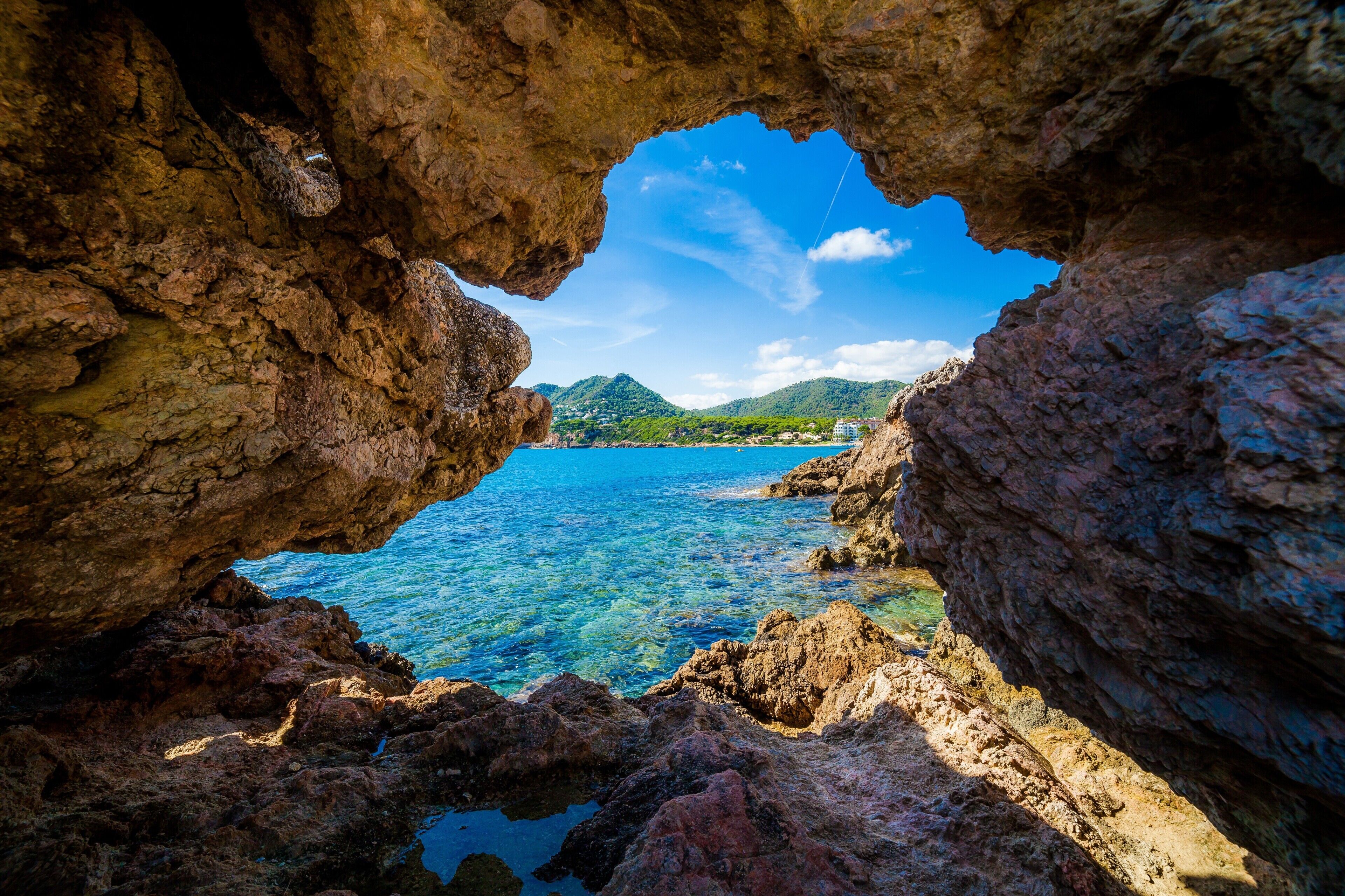 A natural rock formation with a clear view of a coastal area, including water and distant land.