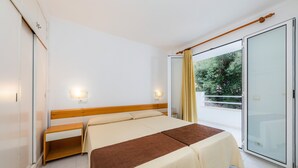 Habitación de hotel con cama, mesitas de noche, armario, puerta de vidrio corredera a un balcón y dos luces fijadas en la pared.