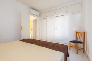 Un dormitorio con cama, una silla de madera, un armario y un aire acondicionado.