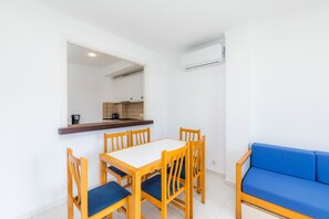 Un área de comedor con una mesa blanca y sillas de madera, un sofá azul y un equipo de aire acondicionado en la pared.