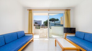 Ein Zimmer mit zwei blauen Sofas, einem Holztisch, einem Fernseher und einer Glastür zum Balkon.