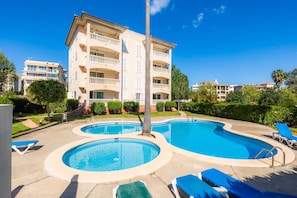 A hotel with a swimming pool, lounge chairs, and a well-maintained garden.