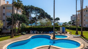 A swimming pool with lounge chairs, palm trees, and a view of the sea. - Apartment 'Oro del Mar IV 01' with Shared Pool, Garden, and Wi-Fi (Canyamel)