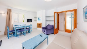 A living room with a sofa, a dining table with chairs, a TV, and a fireplace. - Apartment 'Oro del Mar IV 01' with Shared Pool, Garden, and Wi-Fi (Canyamel)