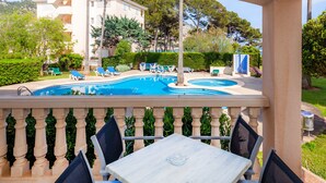A pool area with lounge chairs, a table, and a view of a building in the background. - Apartment 'Oro del Mar IV 01' with Shared Pool, Garden, and Wi-Fi (Canyamel)