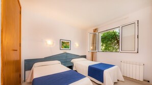 Una habitación con dos camas, un armario de madera, un radiador y una ventana que da a zonas verdes.