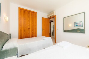 A hotel room with two beds, wooden wardrobes, a mirror, and a wall-mounted picture.