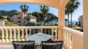 A balcony with a table and chairs, overlooking a coastal area with buildings and palm trees. - Apartment 'Oro del Mar IV 05' with Shared Pool, Shared Garden and Wi-Fi (Canyamel)