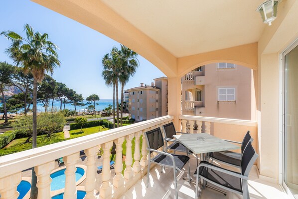 Un balcon avec une table et des chaises, donnant sur une piscine et offrant une vue sur la mer et les bâtiments.