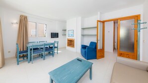 A living room with a sofa, a coffee table, a dining table with chairs, a TV, and a door with a frosted glass panel. - Apartment 'Oro del Mar IV 05' with Shared Pool, Shared Garden and Wi-Fi (Canyamel)
