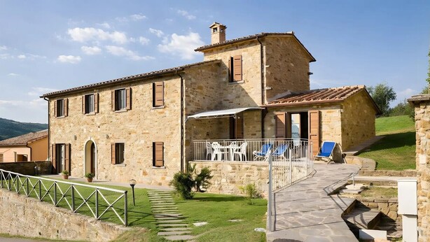 A stone building with a balcony, outdoor seating, and a stone staircase.