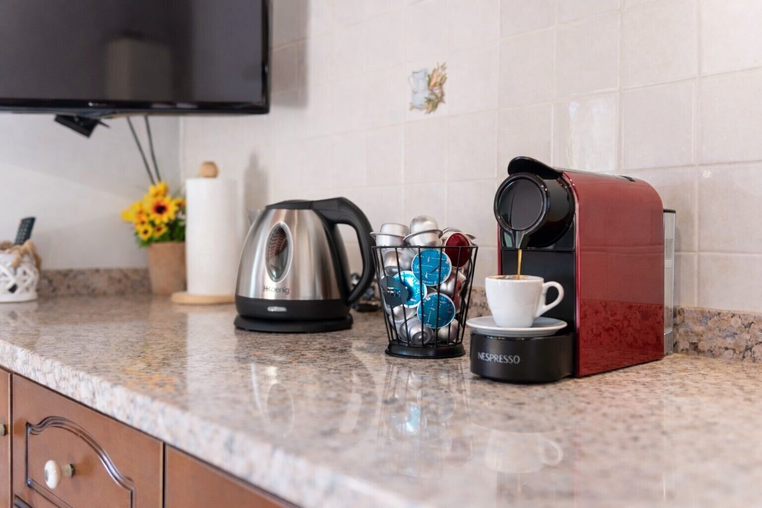 Un comptoir de cuisine avec une machine à café, une bouilloire, un panier de dosettes de café et une tasse de café.