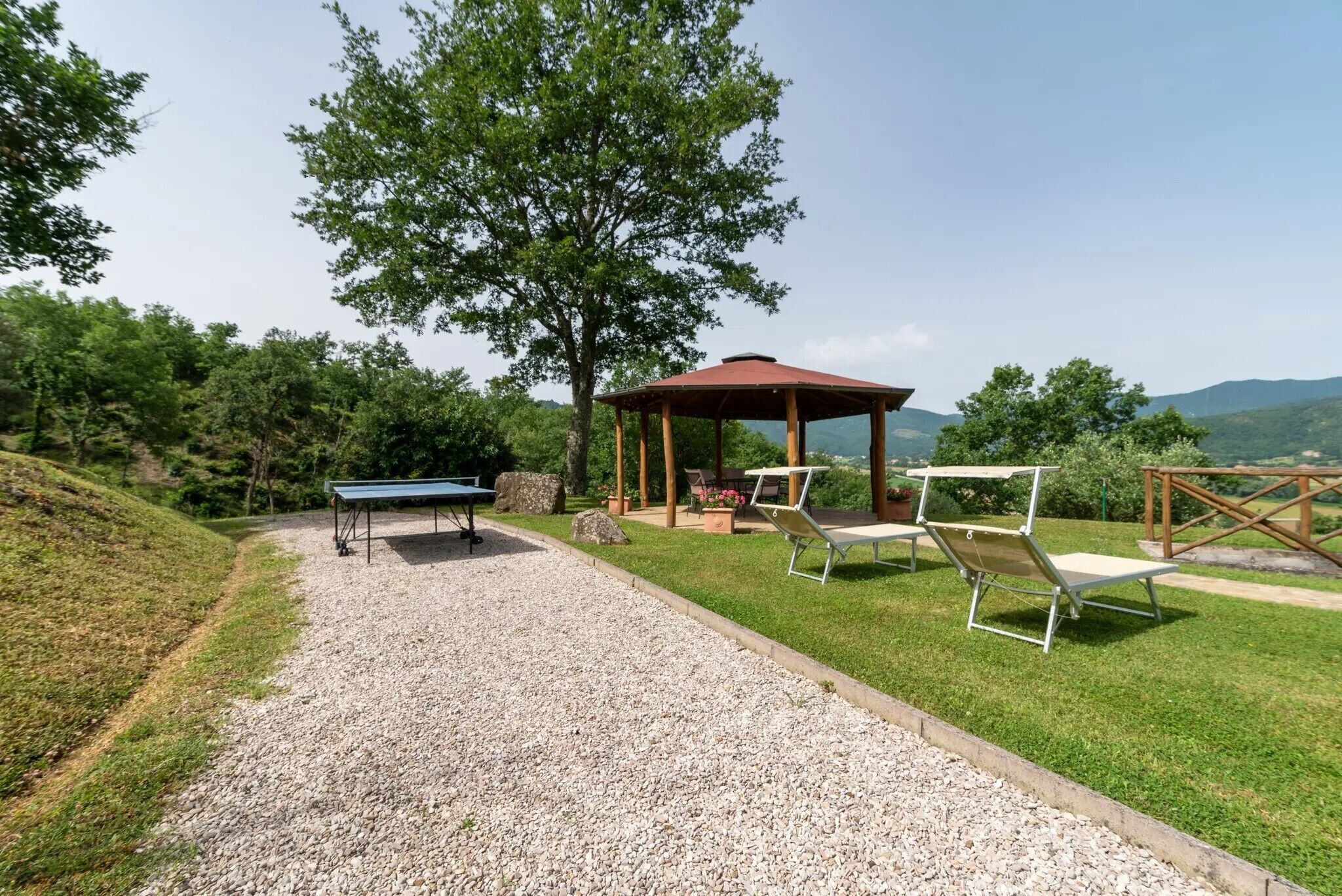 Un mirador, asientos exteriores y una mesa en una zona ajardinada con vistas a colinas.