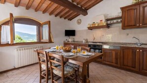 A kitchen with wooden cabinets, a dining table set for breakfast, a window with curtains, and a view of the outdoors.