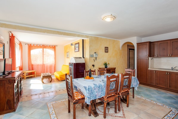 A dining area with a table set for four, wooden chairs, a small side table, and a kitchen area with cabinets and a sink.