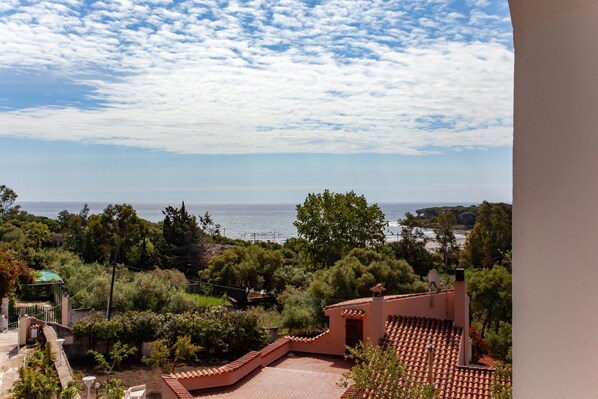 A coastal view with a terracotta-roofed building, lush greenery, and a clear sky.