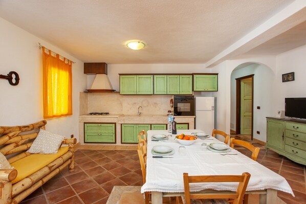 Un comedor con una mesa dispuesta para cuatro personas, armarios verdes, una cocina con electrodomésticos y un banco de madera.