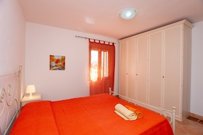 A bedroom with a bed, a nightstand, a painting, a wardrobe, and a window with curtains.