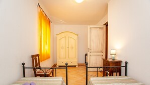 Una habitación con dos camas, una silla, un armario y un escritorio con lámpara.