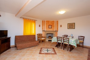A living room with a sofa, TV, dining table with chairs, fireplace, and tiled floor.