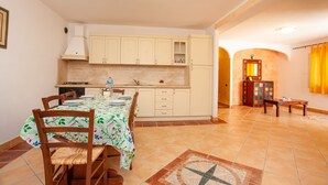 Un comedor con una mesa dispuesta para cuatro personas, una cocina con armarios blancos y piso de baldosas.