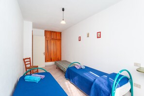 A room with two beds, a wooden wardrobe, a chair, and a small table.