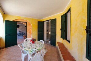 A patio with a table and chairs, a bicycle in the background, and green shutters on the walls.